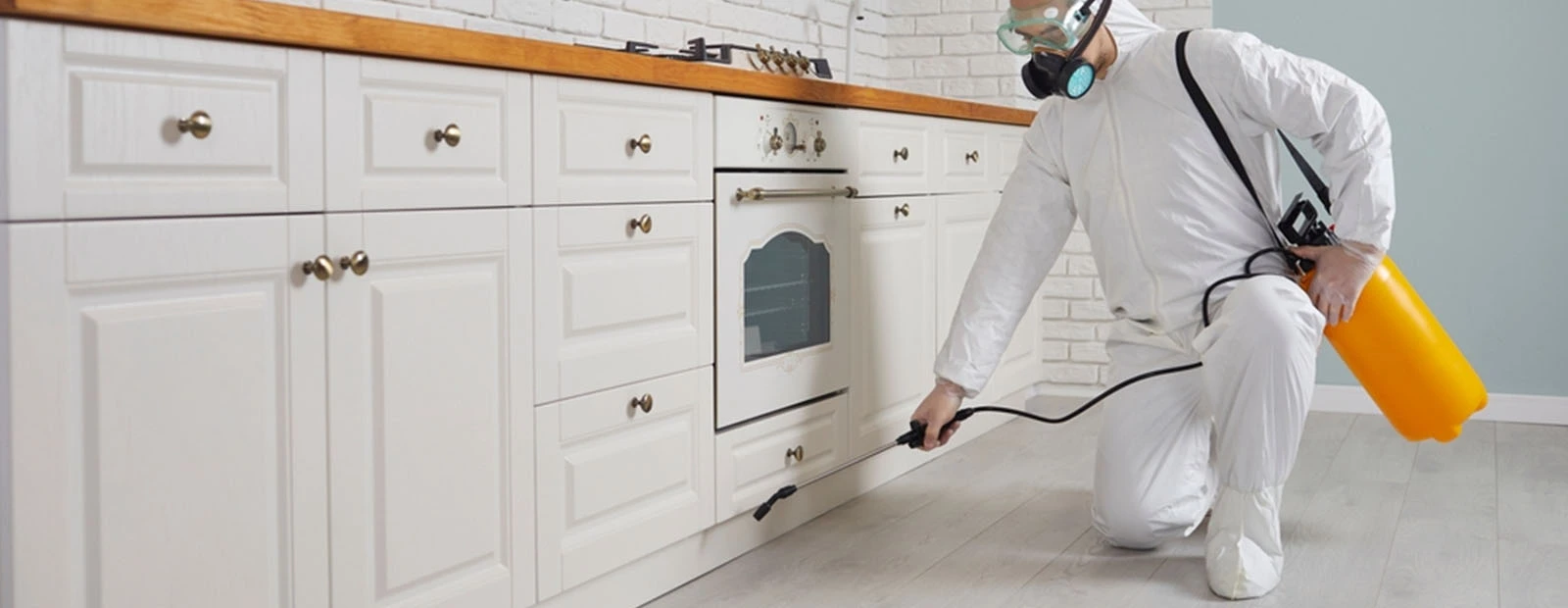 a pest control local worker wearing a white mask holding a foamer cleaning the counter kitchen